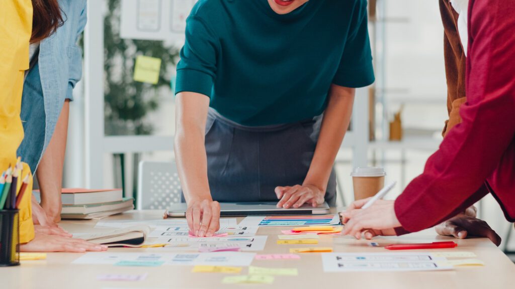 Integración de branding y marketing: un enfoque para el éxito 3 Hombres de negocios asiáticos y mujeres de negocios que se reúnen para intercambiar ideas sobre la aplicación de planificación de diseño web creativo y desarrollar el diseño de la plantilla para proyectos de teléfonos móviles que trabajan juntos en una oficina pequeña